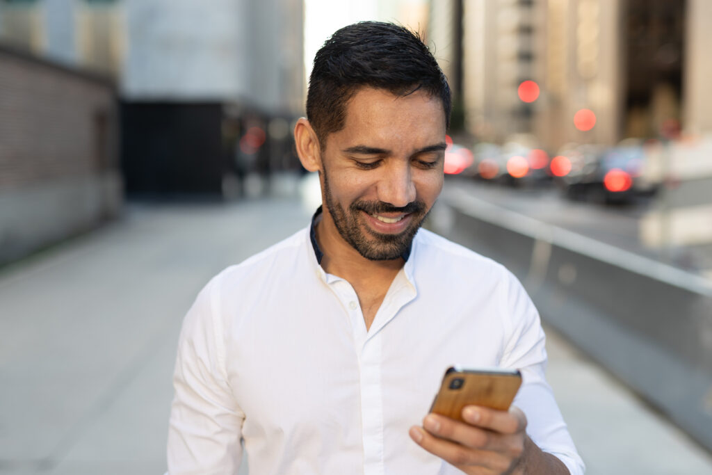 Young Latino Hispanic man in city walking texting cell phone