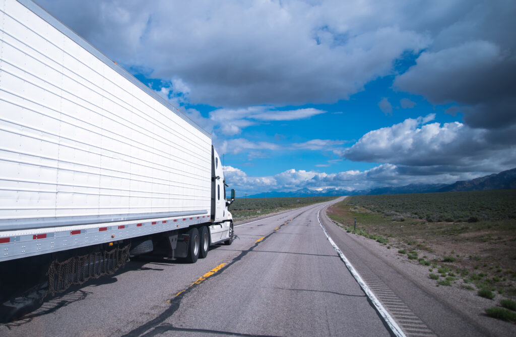 Semi Truck with refrigerated trailer and chains hanging under the trailer moves at high speed on the oncoming lane of the desolate road leaving horizon amid the gentle hills of Arizona